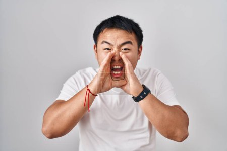 Téléchargez les photos : Young chinese man standing over white background shouting angry out loud with hands over mouth - en image libre de droit