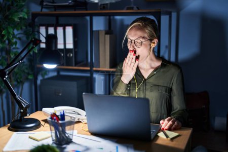 Téléchargez les photos : Young blonde woman working at the office at night bored yawning tired covering mouth with hand. restless and sleepiness. - en image libre de droit