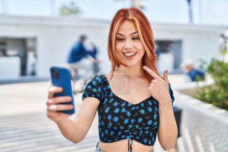 Téléchargez les photos : Jeune femme caucasienne faisant appel vidéo avec smartphone souriant heureux pointant avec la main et le doigt - en image libre de droit