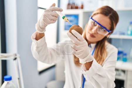 Photo for Young blonde woman wearing scientist uniform injecting on kiwi at laboratory - Royalty Free Image