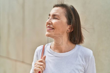 Téléchargez les photos : Femme d'âge moyen souriant confiant regardant le ciel dans la rue - en image libre de droit