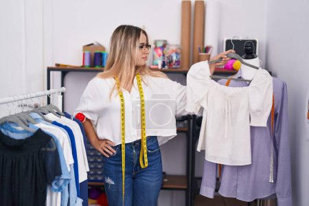 Téléchargez les photos : Young blonde woman tailor smiling confident holding t shirt at clothing shop - en image libre de droit