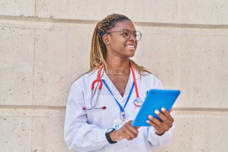 Foto de Médico afroamericano sonriendo confiado usando touchpad en el hospital - Imagen libre de derechos