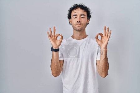 Téléchargez les photos : Homme hispanique debout sur fond isolé détendu et souriant les yeux fermés faisant geste de méditation avec les doigts. concept de yoga. - en image libre de droit