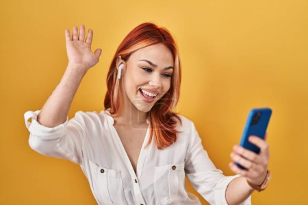 Photo for Young caucasian woman using smartphone wearing earphones celebrating achievement with happy smile and winner expression with raised hand - Royalty Free Image