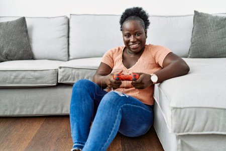 Photo for Young african american woman playing video game sitting on the floor at home - Royalty Free Image