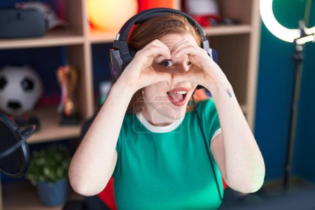 Téléchargez les photos : Young redhead woman streamer smiling confident doing heart symbol with hands at gaming room - en image libre de droit