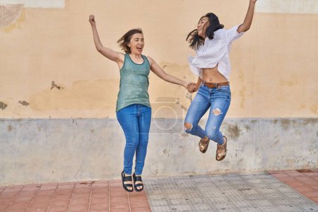 Foto de Two women mother and daughter smiling confident jumping at street - Imagen libre de derechos