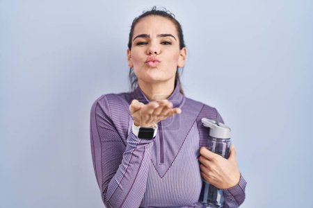Photo for Beautiful woman wearing sportswear holding water bottle looking at the camera blowing a kiss with hand on air being lovely and sexy. love expression. - Royalty Free Image