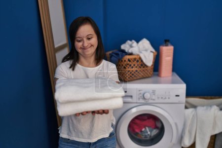 Foto de Síndrome de Down mujer sonriendo confiado sosteniendo toallas limpias en la sala de lavandería - Imagen libre de derechos