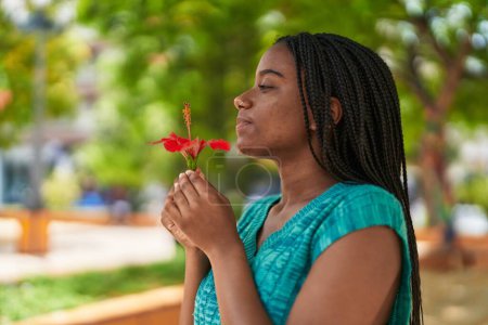 Téléchargez les photos : African american woman smiling confident smelling flower at park - en image libre de droit