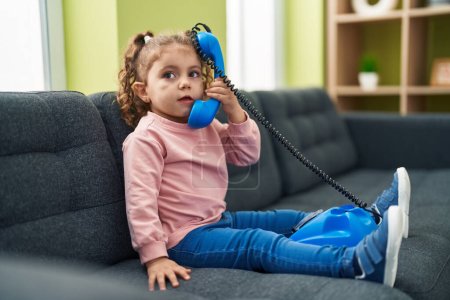 Photo for Adorable caucasian girl playing with telephone toy sitting on sofa at home - Royalty Free Image