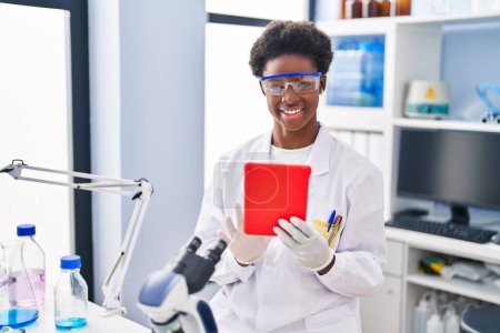 Photo for African american woman wearing scientist uniform using touchpad at laboratory - Royalty Free Image