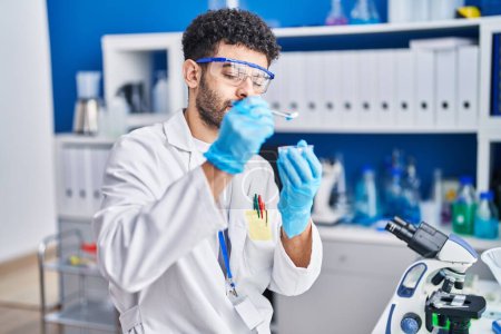 Foto de Hombre árabe joven vistiendo uniforme científico sosteniendo pastillas en el laboratorio - Imagen libre de derechos