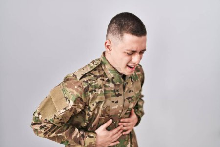 Photo for Young man wearing camouflage army uniform with hand on stomach because indigestion, painful illness feeling unwell. ache concept. - Royalty Free Image