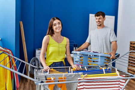 Foto de Hombre y mujer pareja sonriendo seguro colgando clavos en tendedero en la lavandería - Imagen libre de derechos