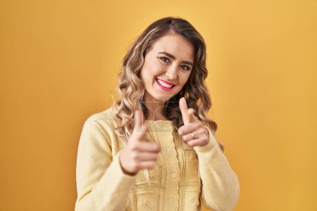 Téléchargez les photos : Jeune femme caucasienne debout sur fond jaune pointant les doigts vers la caméra avec un visage heureux et drôle. bonne énergie et vibes. - en image libre de droit
