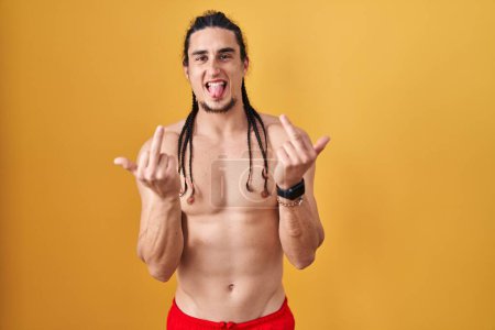 Foto de Hispanic man with long hair standing shirtless over yellow background showing middle finger doing fuck you bad expression, provocation and rude attitude. screaming excited - Imagen libre de derechos