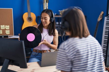 Photo for Two women musicians listening to music holding vinyl disc at music studio - Royalty Free Image