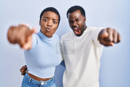 Foto de Joven pareja afroamericana de pie sobre fondo azul señalando disgustado y frustrado a la cámara, enojado y furioso con usted - Imagen libre de derechos