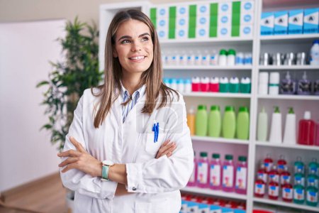Foto de Young beautiful hispanic woman pharmacist smiling confident standing with arms crossed gesture at pharmacy - Imagen libre de derechos