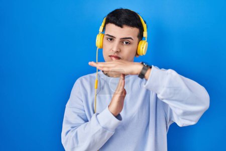 Photo for Non binary person listening to music using headphones doing time out gesture with hands, frustrated and serious face - Royalty Free Image