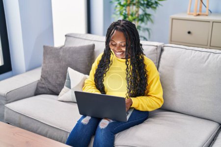Photo for African american woman using laptop sitting on sofa at home - Royalty Free Image