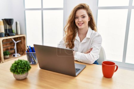 Téléchargez les photos : Jeune femme caucasienne travaillant au bureau en utilisant ordinateur portable visage heureux souriant avec les bras croisés regardant la caméra. personne positive. - en image libre de droit
