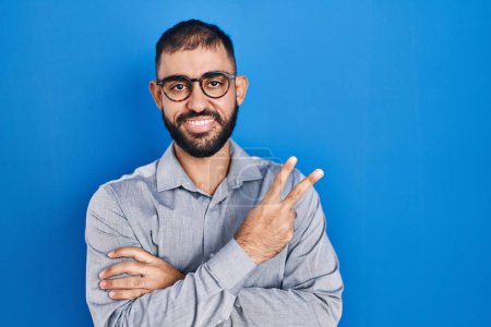 Téléchargez les photos : Middle east man with beard standing over blue background smiling with happy face winking at the camera doing victory sign. number two. - en image libre de droit