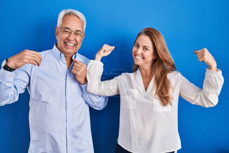 Photo for Middle age hispanic couple standing over blue background showing arms muscles smiling proud. fitness concept. - Royalty Free Image