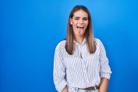 Photo for Hispanic young woman standing over blue background sticking tongue out happy with funny expression. emotion concept. - Royalty Free Image