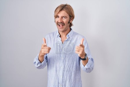Foto de Caucasian man with mustache standing over white background pointing fingers to camera with happy and funny face. good energy and vibes. - Imagen libre de derechos