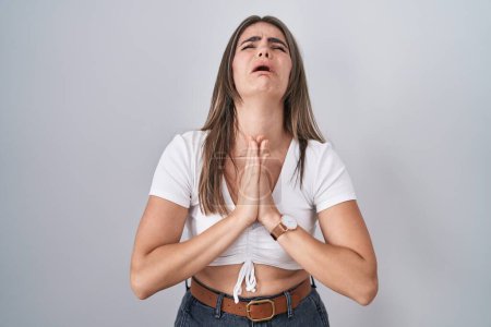 Photo for Young beautiful woman wearing casual white t shirt begging and praying with hands together with hope expression on face very emotional and worried. begging. - Royalty Free Image