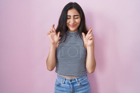 Téléchargez les photos : Young teenager girl wearing casual striped t shirt gesturing finger crossed smiling with hope and eyes closed. luck and superstitious concept. - en image libre de droit