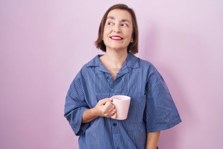 Téléchargez les photos : Moyen Age femme hispanique boire une tasse de café souriant regardant vers le côté et regardant loin en pensant. - en image libre de droit