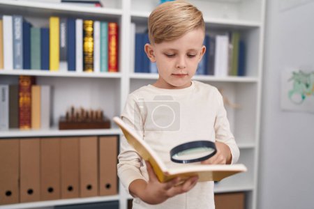 Foto de Adorable libro de lectura de niños pequeños usando lupa en el aula - Imagen libre de derechos