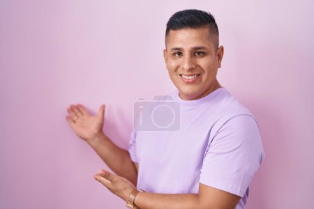 Téléchargez les photos : Jeune homme hispanique debout sur fond rose invitant à entrer souriant naturel avec la main ouverte - en image libre de droit