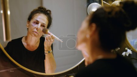 Photo for Middle age hispanic woman using makeup to cover signs of domestic violence at bathroom - Royalty Free Image