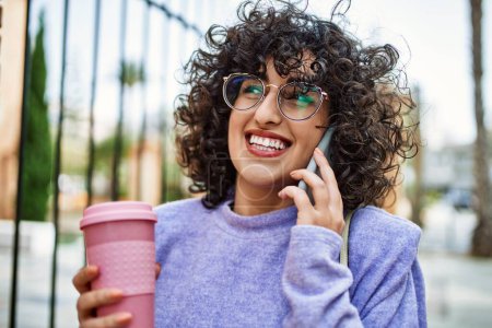 Téléchargez les photos : Jeune femme du Moyen-Orient souriant confiant parler sur le smartphone à la rue - en image libre de droit