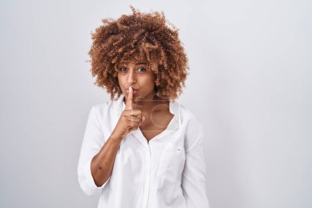 Téléchargez les photos : Young hispanic woman with curly hair standing over white background asking to be quiet with finger on lips. silence and secret concept. - en image libre de droit