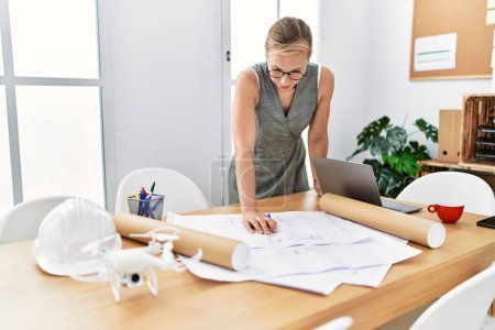 Photo for Young caucasian woman writing on architect plan working at architecture studio - Royalty Free Image