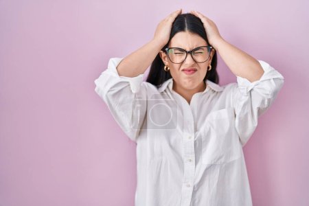 Photo for Young brunette woman standing over pink background suffering from headache desperate and stressed because pain and migraine. hands on head. - Royalty Free Image