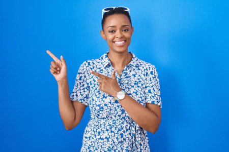 Photo for African american woman standing over blue background smiling and looking at the camera pointing with two hands and fingers to the side. - Royalty Free Image