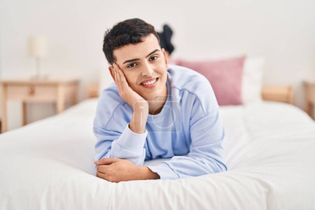 Téléchargez les photos : Jeune homme non binaire souriant confiant couché sur le lit - en image libre de droit
