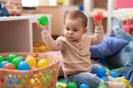 Téléchargez les photos : Adorable tout-petit jouant avec des boules assises sur le sol à la maternelle - en image libre de droit
