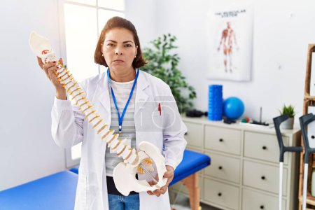 Photo for Middle age hispanic physiotherapy woman holding anatomical model of spinal column skeptic and nervous, frowning upset because of problem. negative person. - Royalty Free Image