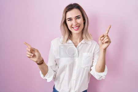 Foto de Young beautiful woman standing over pink background smiling confident pointing with fingers to different directions. copy space for advertisement - Imagen libre de derechos