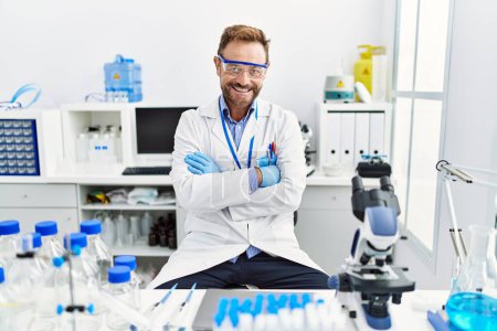 Foto de Hombre de mediana edad que trabaja en el laboratorio científico cara feliz sonriendo con los brazos cruzados mirando a la cámara. persona positiva. - Imagen libre de derechos
