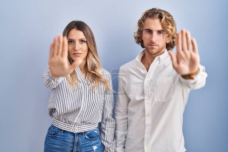 Photo for Young couple standing over blue background doing stop sing with palm of the hand. warning expression with negative and serious gesture on the face. - Royalty Free Image