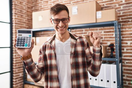 Photo for Caucasian business man working at small business ecommerce holding calculator screaming proud, celebrating victory and success very excited with raised arms - Royalty Free Image